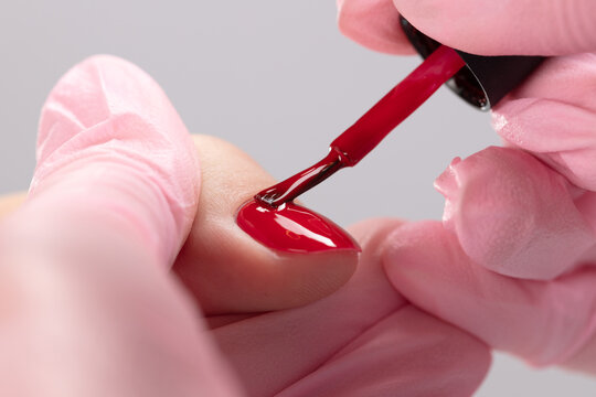 Close up process of applying red varnish. Woman in salon receiving manicure by nail beautician. Red Nail polish and brush, macro. Shallow depth of field