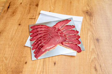 Pastrami slices on aluminum foil sheet on wooden table