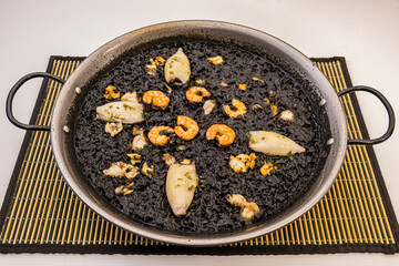 Valencian paella of black rice with squid, prawns and cockles served in its paella pan