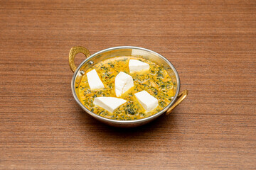 White bowl of palak paneer with spinach and paneer cheese in curry sauce on dark wooden table