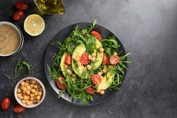 Vegan salad with arugula, vegetables, chickpeas and nutritional yeast flake on dark background with ingredients. Plant-based food concept. flat lay with copy space