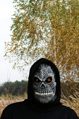 Grim reaper holding halloween pumpkin head. Man in death mask with fire flame in eyes on nature...