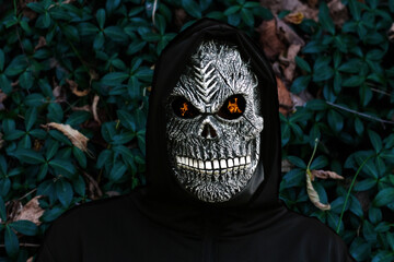 Close-up portrait of grim reaper. Man in death mask with fire flame in eyes on dark emerald...