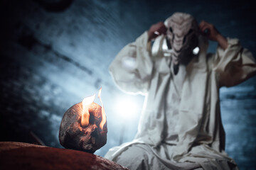 the plague doctor. cosplay of a gloomy image for Halloween. a mask with a bird's beak and a white hoodie. a masked man stretches his hands towards a human skull with burning eyes