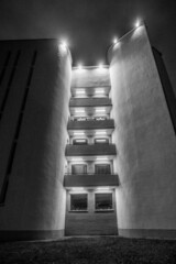 Photo of a gray building with windows and balconies at night with glowing lights