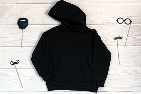 Black Kid Sweatshirt With Hood On White Background Top View. Blank Flat Lay Black Kids Hoodie On White Wooden Backdrop With Christmas Props, Unisex Winter Apparel Mockup