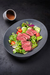 Modern style traditionell gebratene dry aged Bison Rump Steak Scheiben mit Gemüse, Salat und Senf Dressing serviert als close-up auf einem Design Teller mit Textfreiraum  