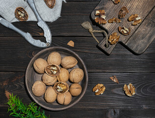 Whole ripe walnuts lie in a wooden plate. Nutshells and nutcrackers on dark wooden boards. Peeled nuts on a board in the background