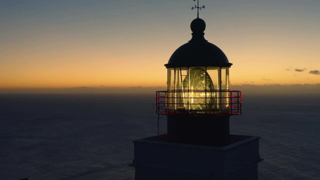Aerial panoramic view of glowing lighthouse at sunset with ocean in the background