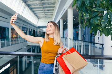 young happy after shopping woman talking on cell in mall. Satisfied joyful female shopaholic with gift colored paper bags in hands. Mobile phone conversation. Smiling joy Stand ang sincerely tells