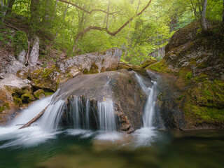 small river deep in the green woods. wonderful springtime scenery of mountains countryside. clear water among forest and rocky shore. wooden fence on the river bank.