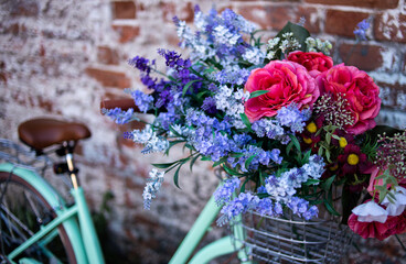 City bike near a brick wall. Bike with a bouquet in a basket. Bike leaning against the wall.