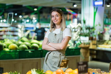 Portrait young woman worker in a Vegetable section supermarket standing smiling with arms crossed....