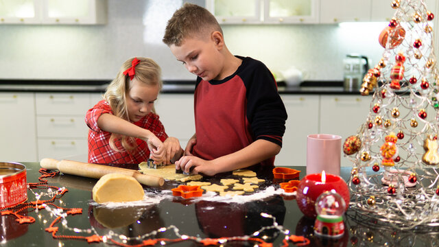 A brother helps his sister bake cookies for the Christmas holiday. They cook together amicably in the kitchen. Cookies for Christmas and New Year. Lifestyle.