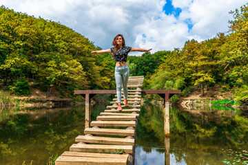Naklejka premium A young woman on a wooden ladder bridge on a forest mountain lake. Amazing summer landscape with a lake and a panoramic view of a mountain lake