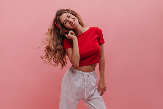 Shining young european girl listening to lovely summer music tracks with copy space. Posing with her new red headphones in crop top and white pants developing blonde hair. Positive emotion concept