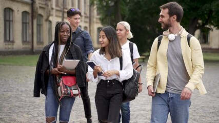 Cheerful multinational high school students chatting while walking through campus park before classes. Positive multi-ethnic friends communicating while going along university park before lessons - Powered by Adobe