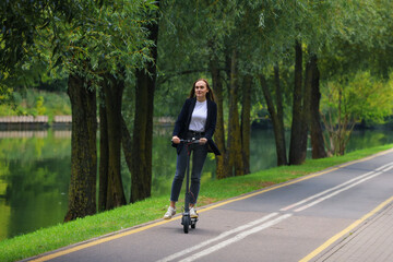 A young woman in stylish clothes rides an electric scooter on a bike path