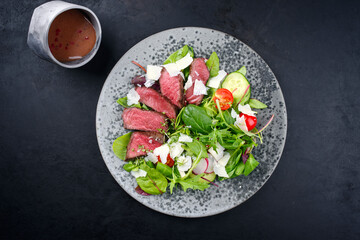 Modern style traditional fried dry aged bison beef rump steak slices with vegetable, lettuce and parmesan cheese served as top view on a Nordic design plate with copy space