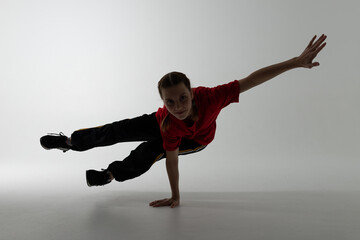 young Russian female hip hop break dancer dancing on grey background, in darkness performing back side one hand stand element of downrock breakdance.