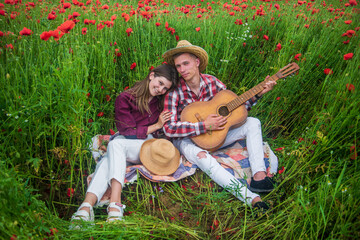 Happy couple in love relax in beautiful field of poppy flower with acoustic guitar, country music