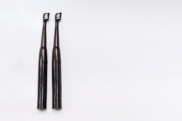 two black electric toothbrushes on a gray background