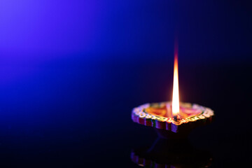 Illuminated Mitti ka Diya With Reflection In Dark Black Background with Blue Gradient. Indian Festival Theme For Diwali Pooja, Navratri, Dussehra Puja, New Year, Deepawali Or Shubh Deepavali