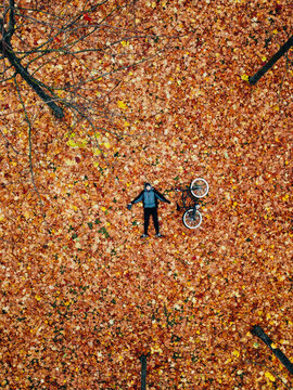 Man laying on yellow leaves in fallen autmn park with bicycle. Aerial shot from above in october yellow fallen park