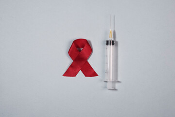 Clean syringe and red ribbon bow as symbol of AIDS and HIV awareness day.
