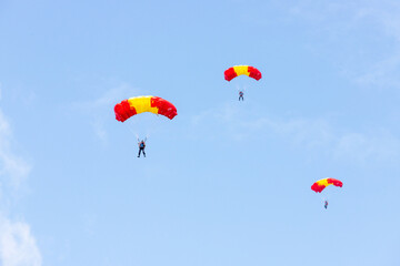 Skydivers under yellow and red parachute dome