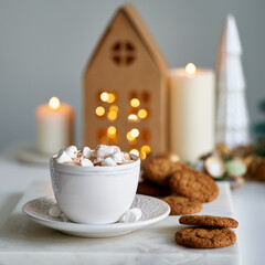 Cozy home Christmas atmosphere, festive holiday mood. Light gray background. Kraft paper house. Homemade chip cookies and cup of hot chocolate. Selective focus, blurred background