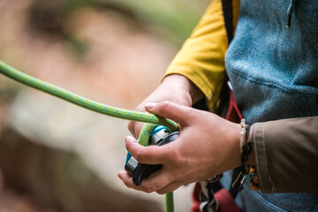 Hands of a climber holding a belay device and a rope while belaying a lead climber.