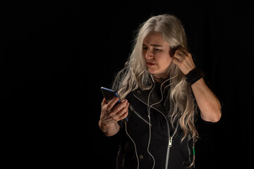 Woman with gray hair and rocker style clothes putting on the headset to listen to music on her cell...