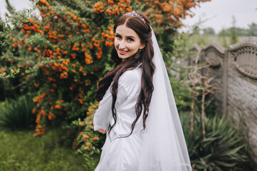 A beautiful, smiling bride model with curly hair in white lingerie, underwear walks, dances in nature, turning around in the park on green grass against a background of orange rowan. Wedding portrait.