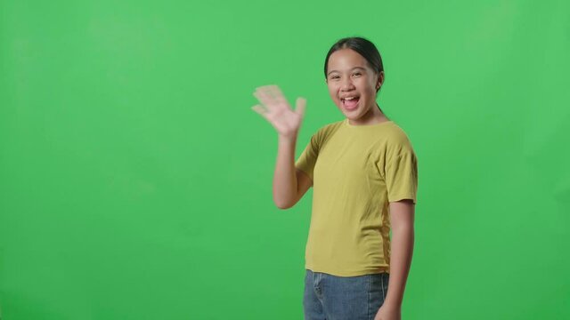 The Happy Young Asian Kid Girl Walking And Waving Hand,Say Bye Bye While Standing On Green Screen In The Studio
