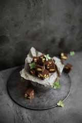 Chocolate candies with pistachios on a small ceramic stand on a gray background. Milk Chocolate Square Sweet Bars with Nuts.