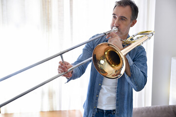 Trombonist practicing trombone in room with curtain background at home