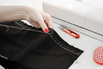 Women's hands with red manicure sew trousers. Basting seam, handmade. There are thread cutters...