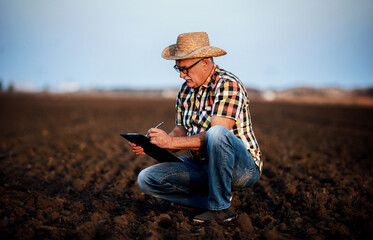 Farmer controls the soil and making a notes before sowing in the field. Agricultural concept