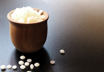 Natural white beeswax granules in a wooden cup. Black background