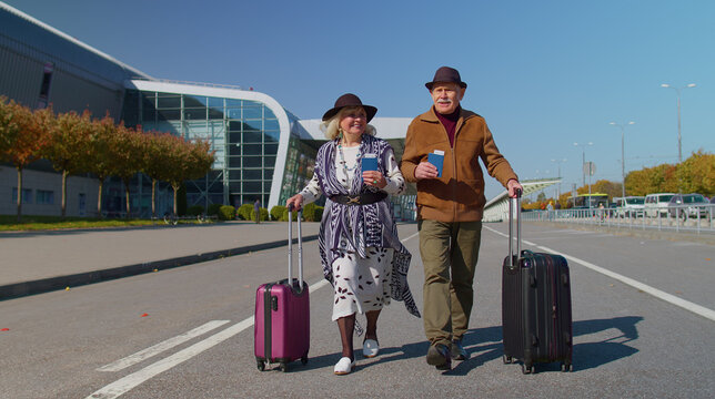 Elderly old husband and wife retirees tourists go to airport terminal for boarding or railway station for traveling. Lovely mature couple grandmother grandfather carrying luggage, tickets, passports