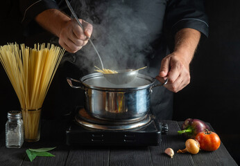 Professional chef prepares Italian pasta in a saucepan with vegetables. Close-up of cook hands while cooking in restaurant kitchen