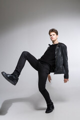 full length portrait of young fit man in dark cloths on the white background. Young Male Fashion Model Posing In Casual Outfit. Attractive young fashion model wearing black in leather jacket