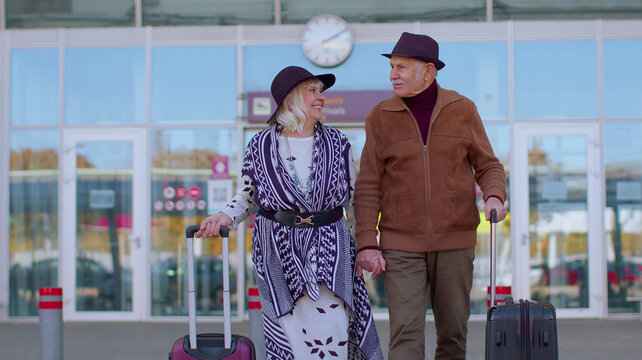 Lovely stylish elderly old retired family grandmother grandfather walking with luggage suitcase bags from airport hall or railway station. Travel, vacation, journey, trip, holidays. Talking, smiling