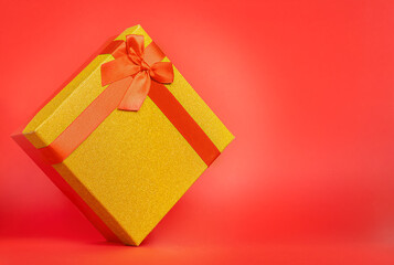 Gold gift box with red ribbon on a red background with a copy space. Concept of sale and preparation for the holiday