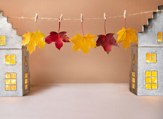 House shaped lanterns with colourful autumn leaves on beige background. Autumn post card with copy space