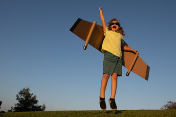 Kids leader and winner, success start up. Excited child boy play with toy jetpack wings superhero in park.