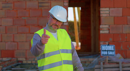 Builder engineer architect looking approvingly at camera showing thumbs up, like sign positive something good at construction site. Foreman worker at building house. Real estate, business, investment