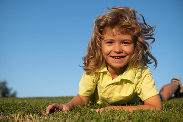 Naklejka na ściany i meble Portrait of a smiling child lying on green grass. Cute kid boy enjoying nature outdoors. Healthy carefree kid playing outside in summer park. Healthy kids outdoor lifestyle concept.