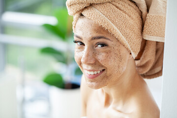 Young beautiful girl applying facial scrub mask on skin.